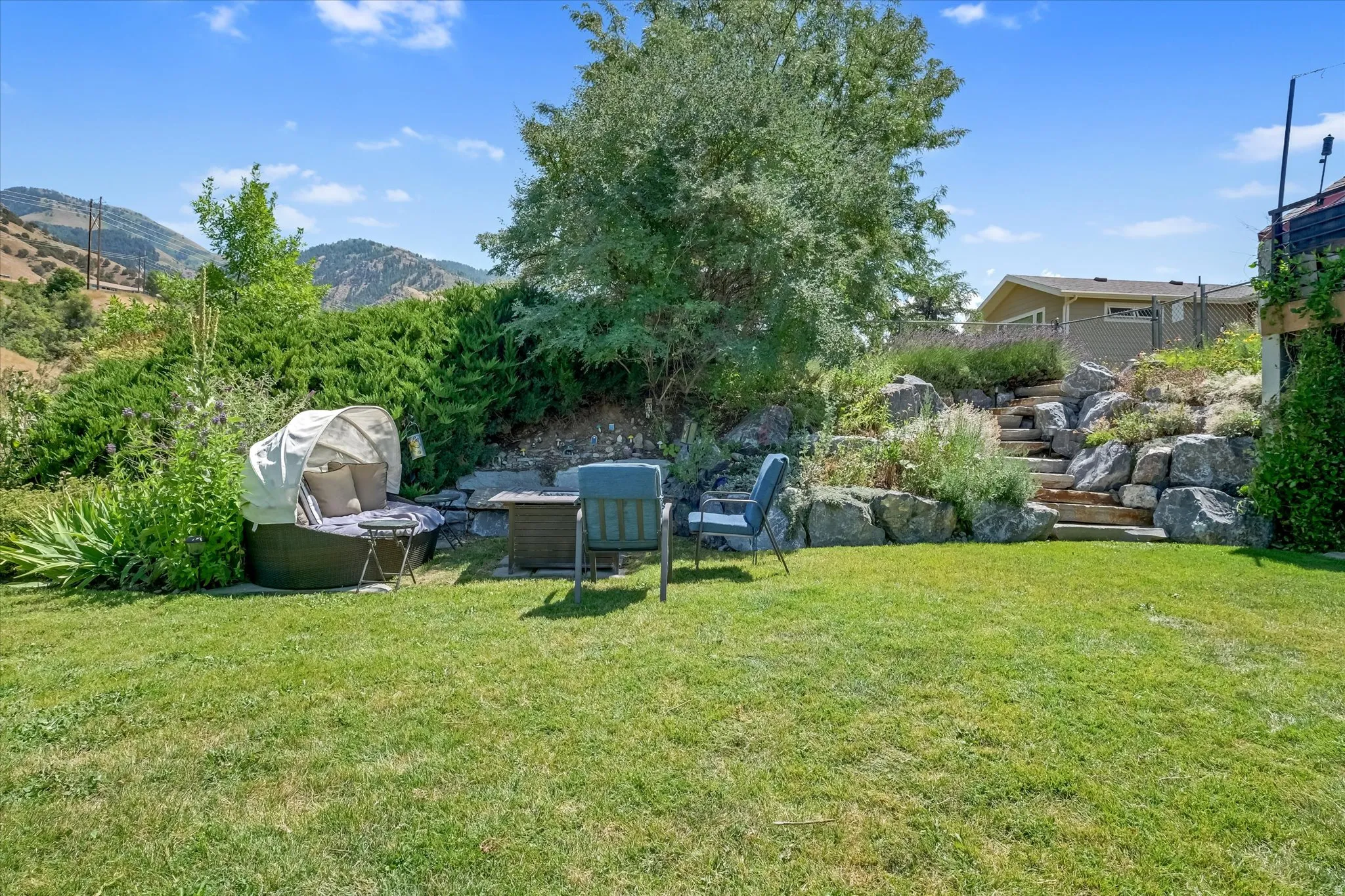 Expansive grassy yard with tiered rock landscaping and natural wood steps