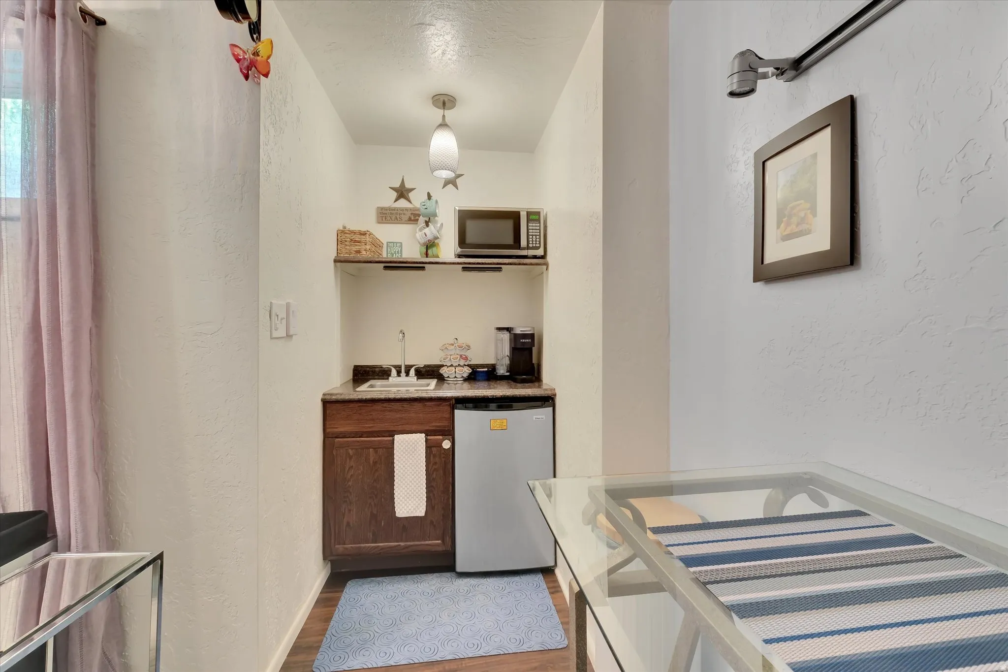 Compact kitchen area featuring a built-in microwave, under-counter refrigerator, sink with faucet, wood-finish cabinetry, and overhead shelving