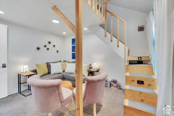 Carpeted living area featuring recessed lighting, a built-in wooden staircase with integrated lighting, and a white interior door with dark hardware