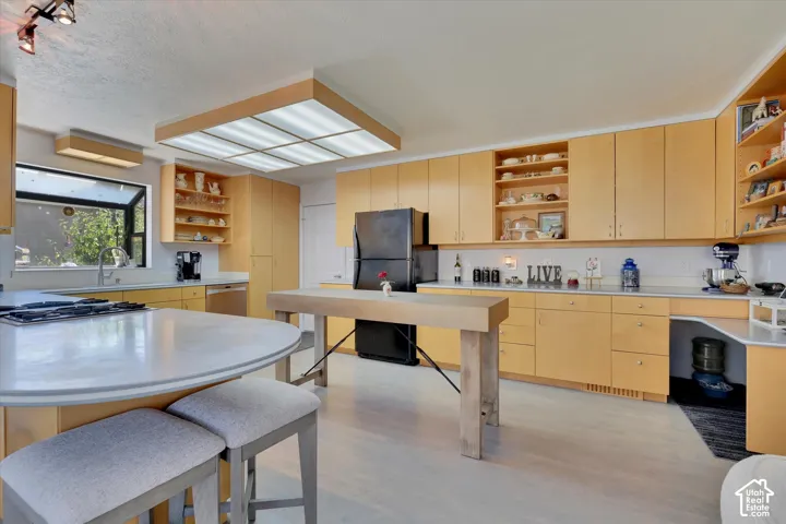 Kitchen featuring extensive light wood cabinetry, a large central island with integrated cooktop, a secondary butcher block island, and a skylight-style ceiling fixture