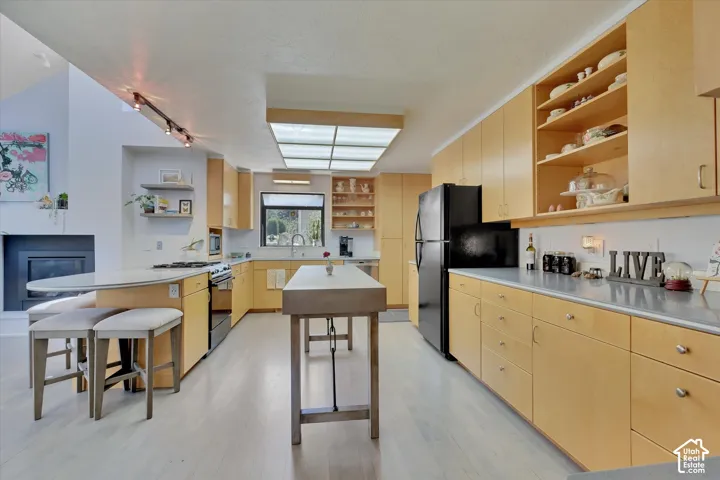 Expansive kitchen featuring light wood-finish cabinetry, black appliances, light-toned countertops, and a skylight