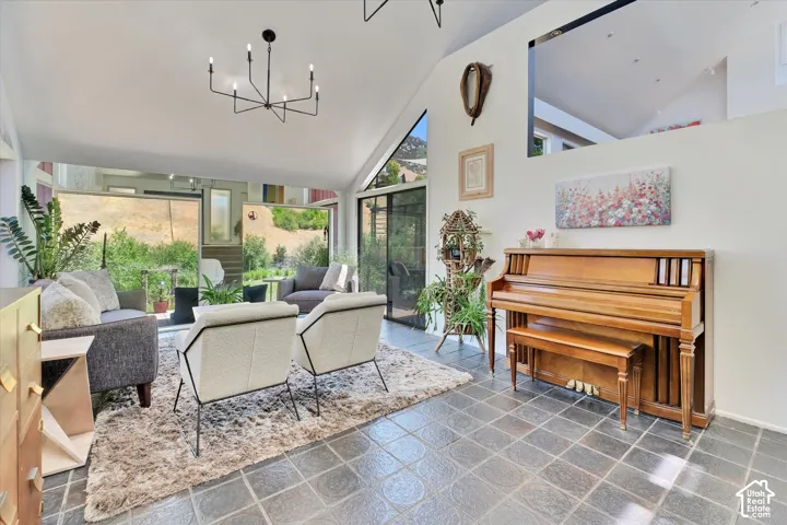 Spacious living area featuring a vaulted ceiling with a contemporary chandelier, large windows, slate tile flooring, and white walls