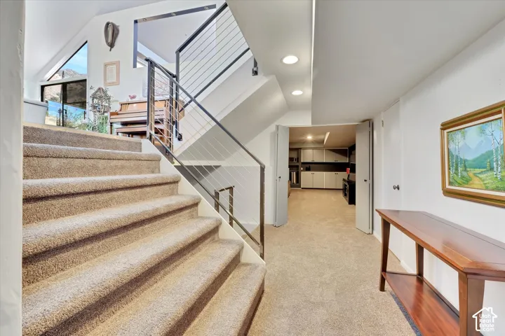 Carpeted staircase featuring a modern cable railing system and recessed lighting