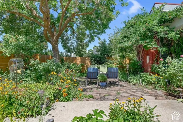Mature trees shade an expansive backyard featuring a stone patio and vibrant garden beds