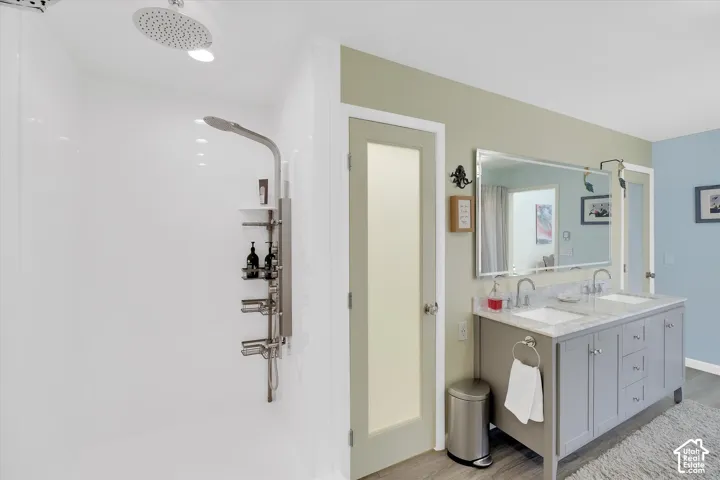Bathroom featuring a dual vanity with undermount sinks and a stone countertop, a large framed mirror, and a walk-in shower with a rain shower head and a multi-function shower panel