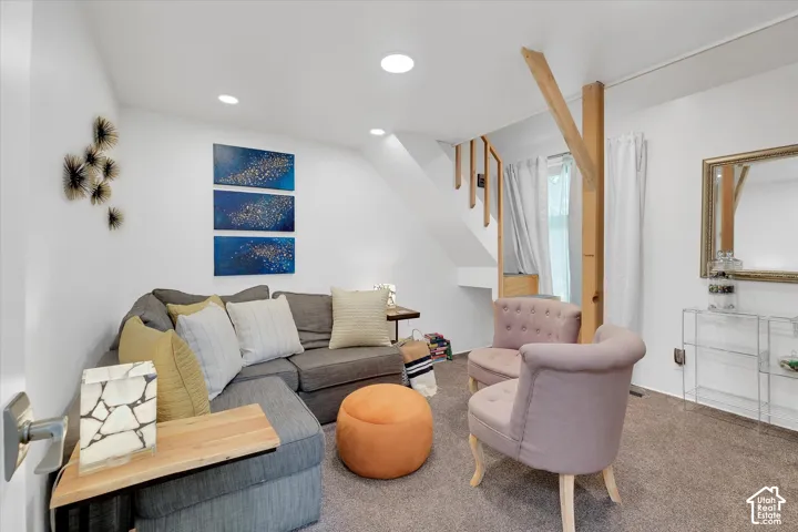 Carpeted living space featuring recessed lighting, white walls, and an exposed wooden support beam