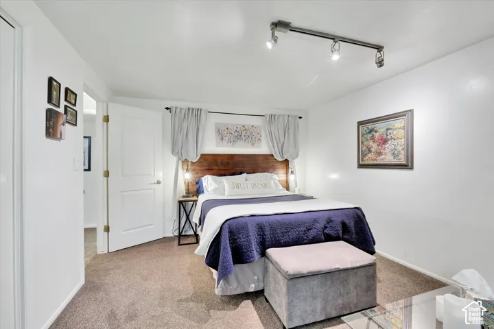 Carpeted bedroom with a built-in wood headboard, white walls, and track lighting