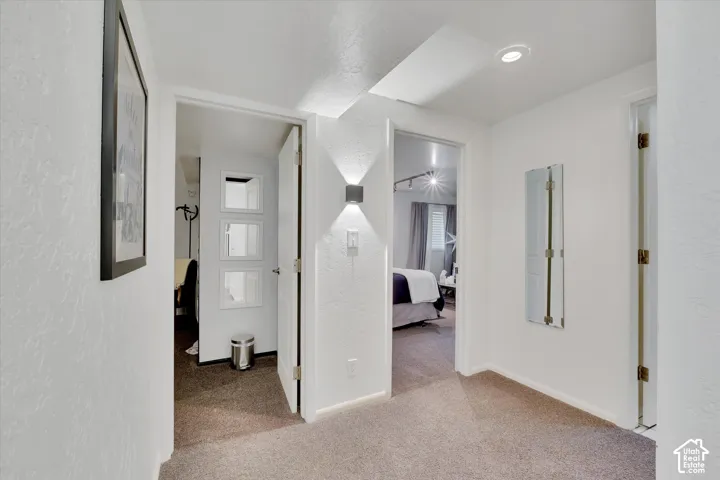 Carpeted hallway with white walls and overhead recessed lighting