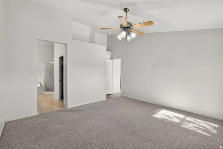 Spacious room featuring vaulted ceilings, a ceiling fan with integrated lighting, and neutral-toned carpeting
