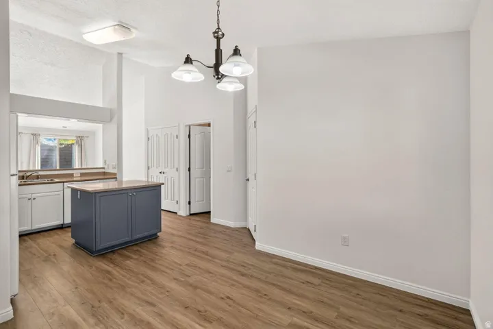 Open-concept living area featuring wood-finish flooring, a kitchen island with storage, white base cabinets, and a decorative chandelier