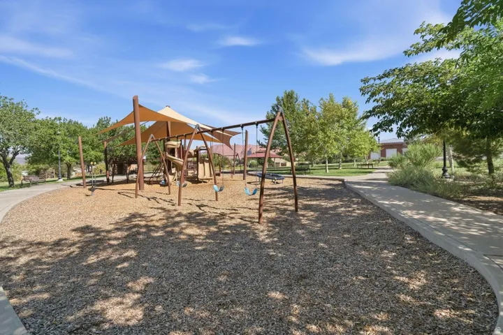 Community playground featuring shade structures, swings, and play equipment on a wood chip base