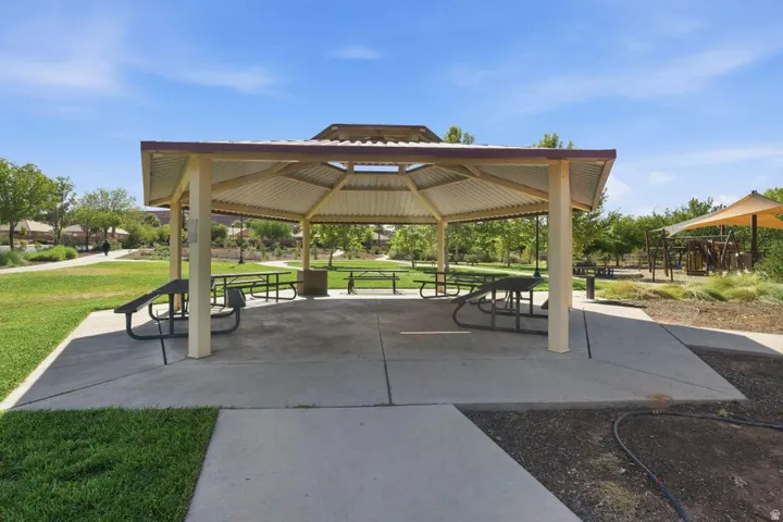 Open-air gazebo with metal roofing and picnic tables, surrounded by manicured lawns and concrete pathways