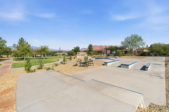 Public park featuring a concrete skate park, paved walking paths, a covered gazebo, mature trees, and a picnic table
