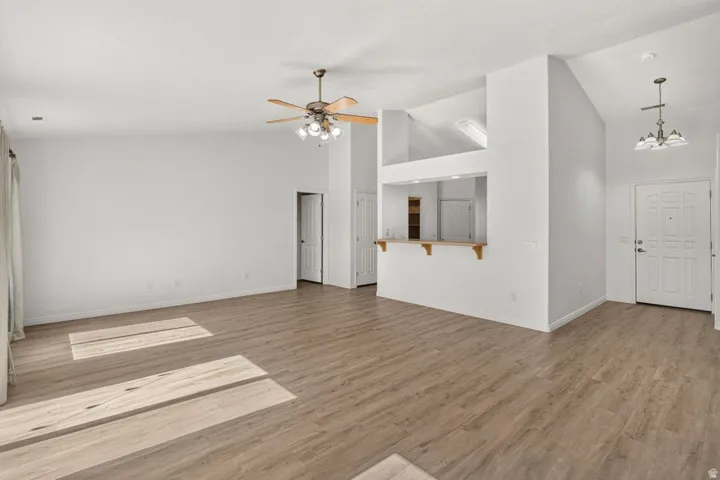 Spacious living area featuring wood-finish flooring, vaulted ceilings, and a ceiling fan with integrated lighting