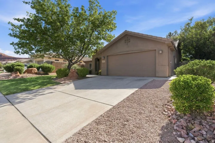 Exterior featuring a concrete driveway, attached garage, stucco siding, and mature landscaping with shrubs and trees