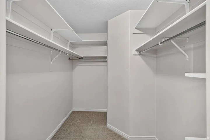 Walk-in closet featuring light beige walls, white shelving, metal hanging rods, and neutral carpet flooring