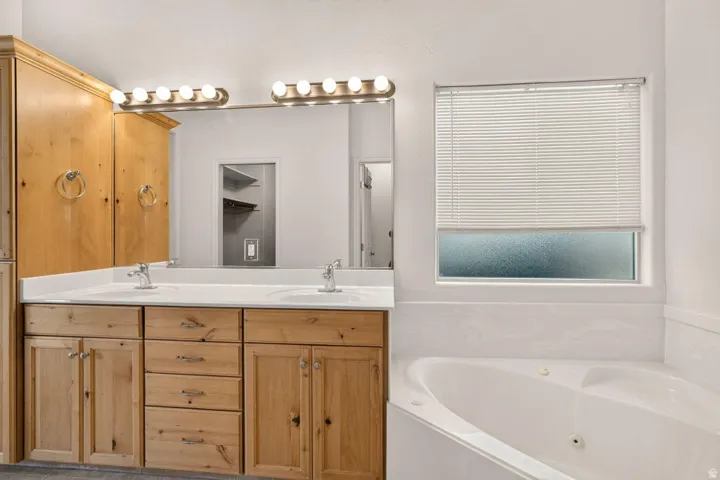 Dual vanity with light wood cabinetry and integrated sinks, complemented by a large mirror and overhead bar lighting