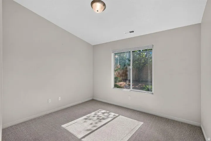 Carpeted room featuring neutral wall tones, a large window with white blinds, and an overhead flush-mount light fixture
