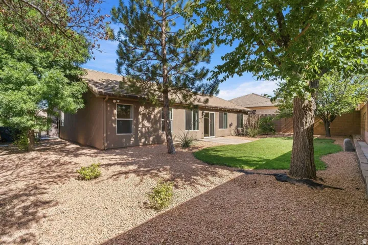 Expansive backyard featuring a central lawn, a large paver patio, mature trees, and gravel landscaping