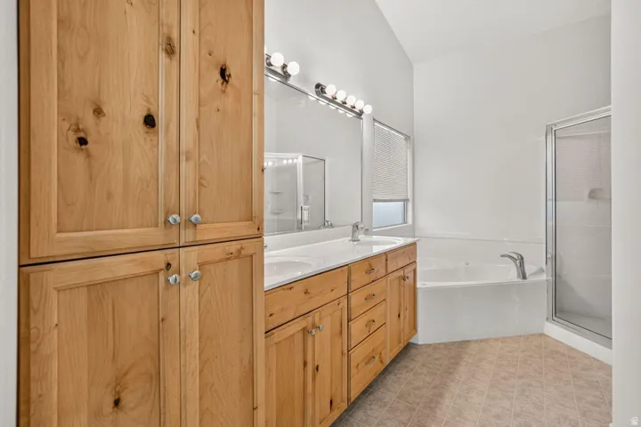 Bathroom featuring natural wood cabinetry, dual vanity with undermount sinks, built-in soaking tub, separate glass-enclosed shower, and vaulted ceiling