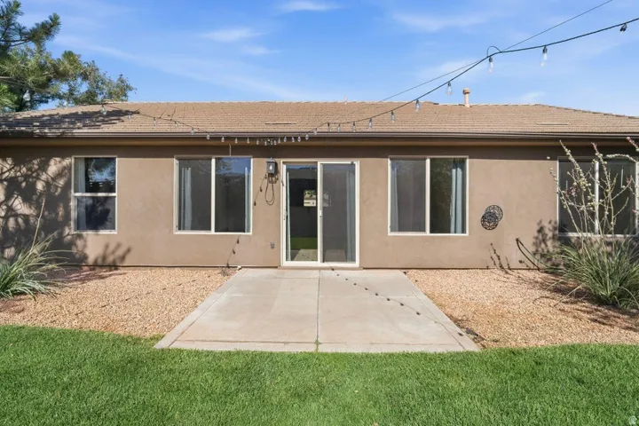 Rear exterior featuring a tan stucco finish, multiple windows, a sliding glass door, and a concrete patio