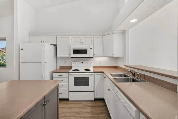 Kitchen featuring vaulted ceilings, white cabinetry, a built-in microwave, white appliances, and wood-finish flooring