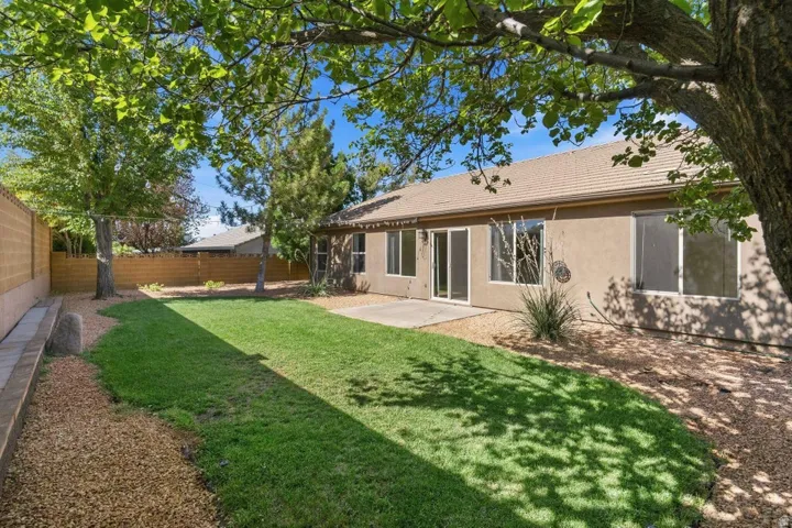 Expansive rear yard featuring a manicured lawn, established trees, and a concrete patio