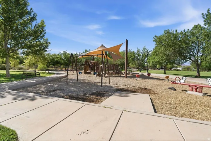 Community playground featuring swings, a shaded play structure, and seesaws on a wood chip base