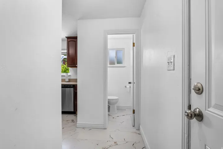 White-painted interior hallway featuring a door with satin nickel hardware and a powder room with white tile flooring