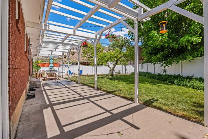 Expansive concrete patio with a white pergola, offering dappled shade