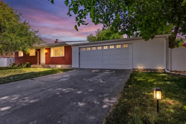Mid-century modern residence featuring a red brick facade, an attached two-car garage with paneling and upper window inserts, a concrete driveway, and landscape lighting