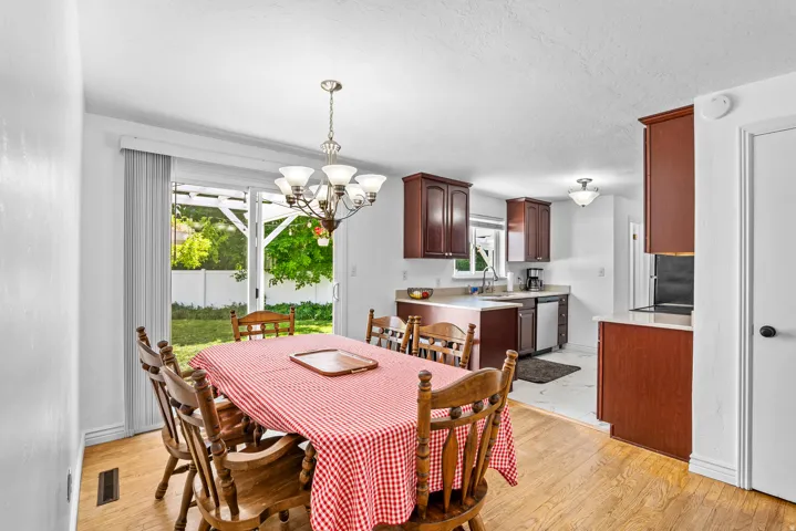Open-concept dining area with wood-finish flooring, a contemporary chandelier, and direct access to the outdoor space via a glass sliding door