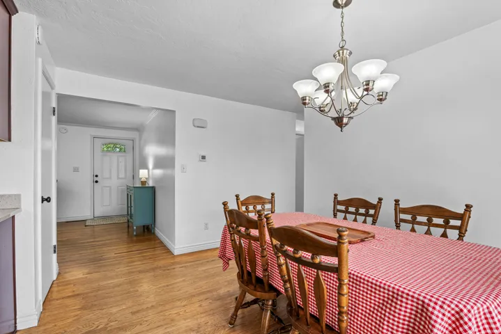 Dining area featuring a brushed nickel chandelier with frosted glass shades, wood-finish flooring, white baseboards, and a white entry door with a decorative glass insert