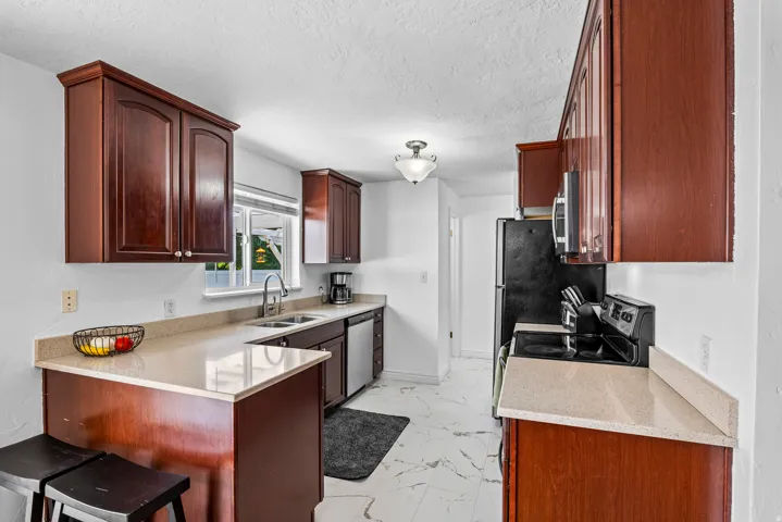 Kitchen featuring dark wood-finish cabinetry, light-toned countertops, a stainless steel sink, a window over the sink, and white-finish flooring