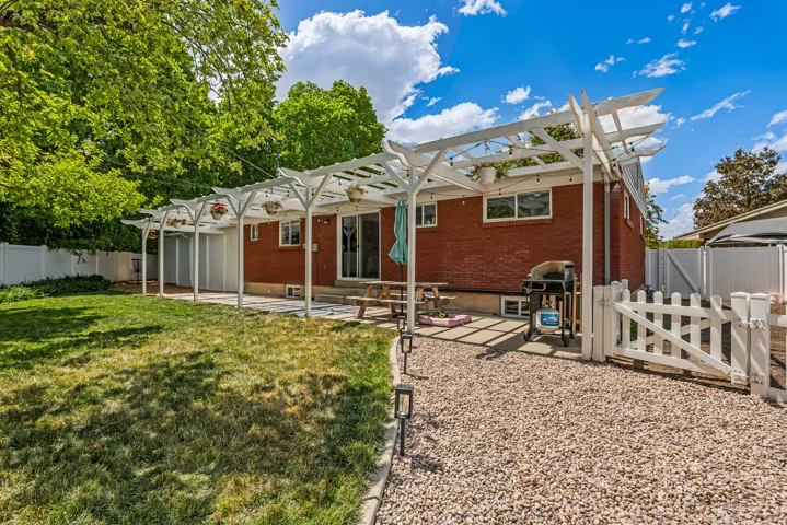 Expansive backyard featuring a red brick exterior, a white pergola-covered patio, a white picket fence, a white privacy fence, and mature trees