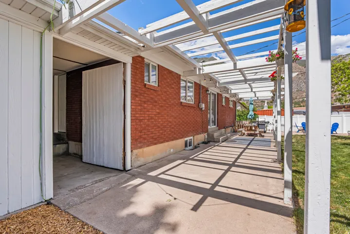 Expansive concrete patio featuring a white pergola extending along the brick exterior