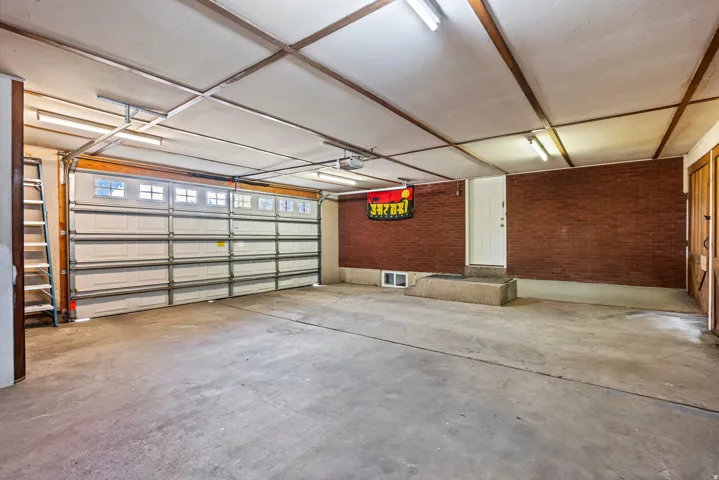 Spacious two-car garage featuring a concrete floor, red brick wall accents, and an overhead garage door with window inserts