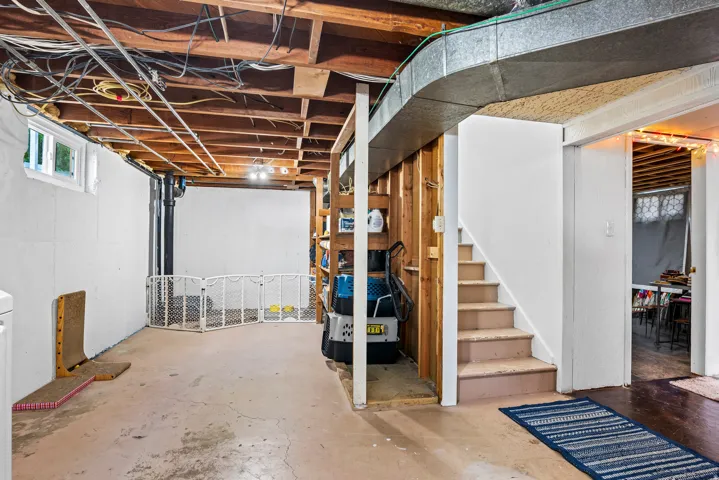 Unfinished basement offering exposed ceiling joists, concrete flooring, painted white foundation walls, and an interior stairway