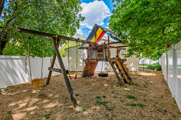 Backyard featuring a wooden playset with slide and swing structure, surrounded by wood chip ground cover