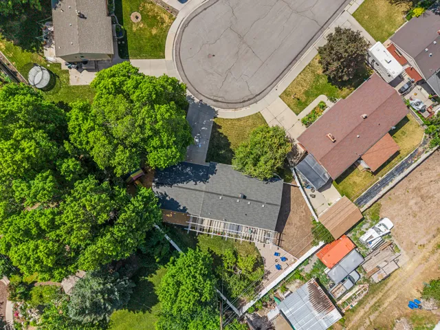 Overhead property view featuring a dark shingle roof, a rear wooden deck, and extensive mature trees
