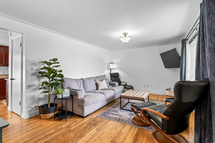 Bright living area featuring wood-finish flooring, white walls, crown molding, and a flush mount ceiling light