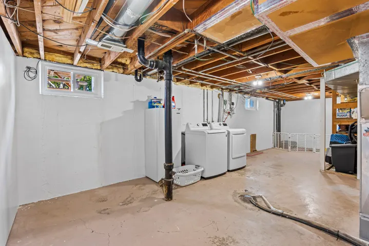 Unfinished basement featuring exposed wood joists, concrete flooring, a single window, and visible plumbing and ductwork