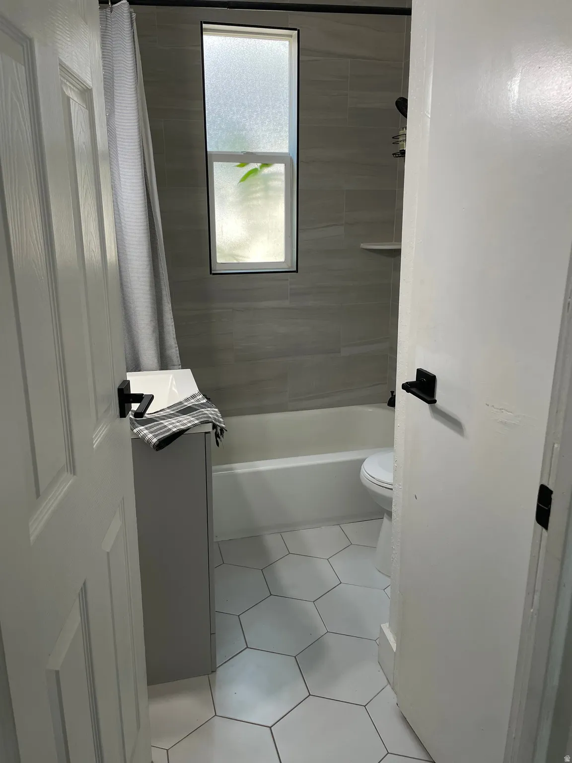 Bathroom featuring a white bathtub, gray tiled walls, white hexagonal floor tiles, and a privacy window