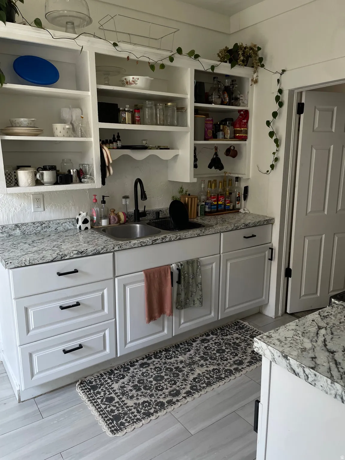 Kitchen featuring white shaker-style cabinetry, patterned stone countertops, and a dual basin sink with a matte black faucet