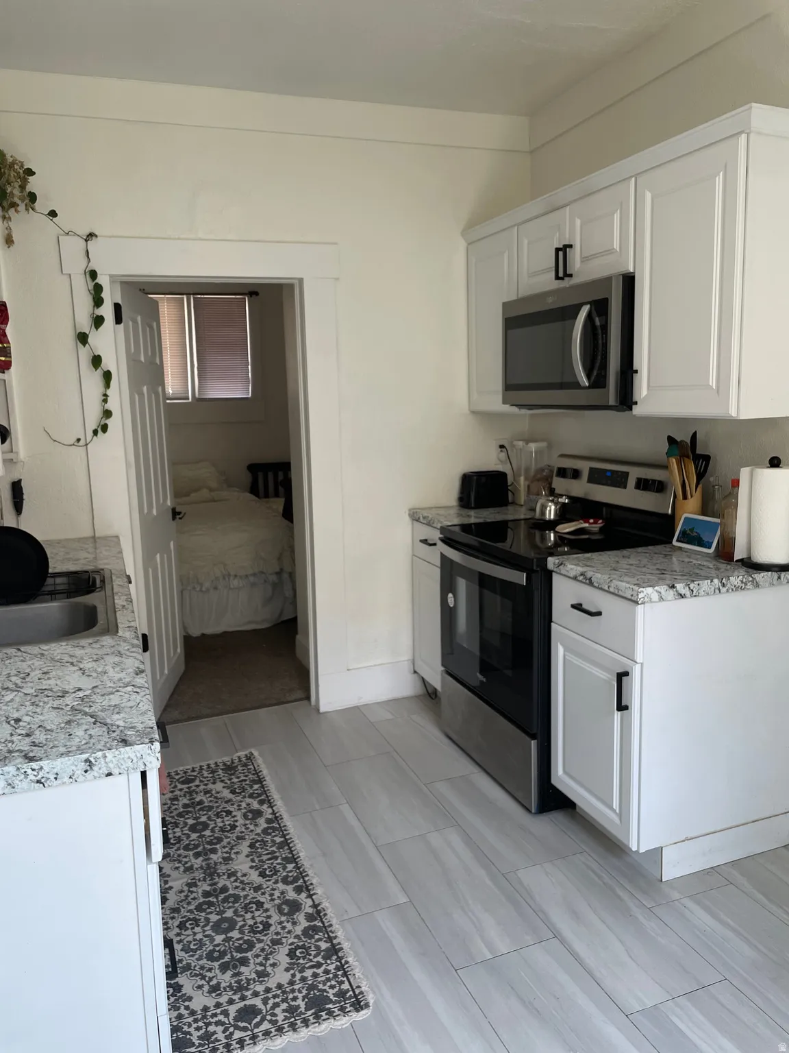 Kitchen featuring white shaker cabinetry, stainless steel appliances, granite countertops, and wood-finish tile flooring