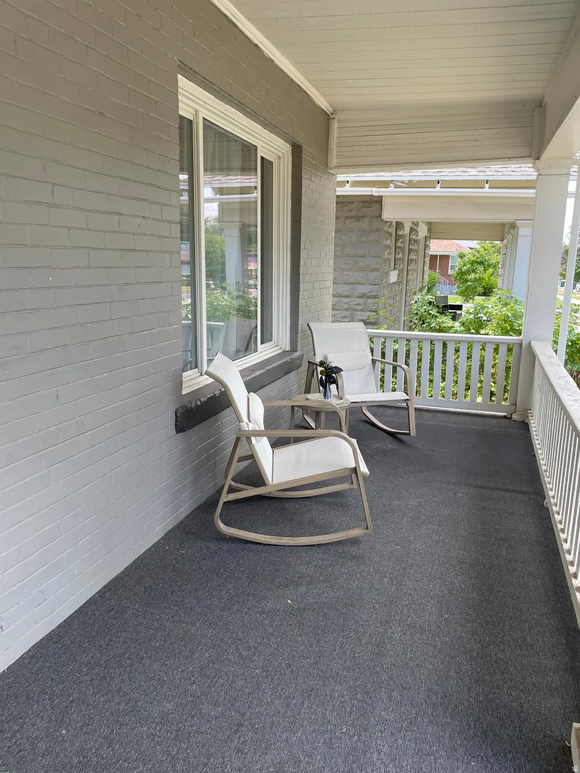 Covered front porch featuring a gray brick exterior, white window trim, white porch railing, and a gray floor