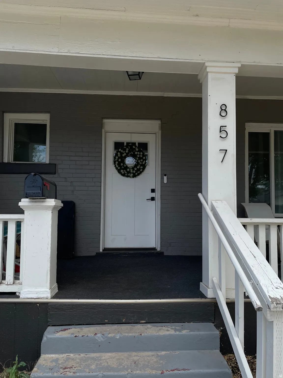 Front porch featuring a white entry door with frosted glass paneling, a dark grey painted brick facade, white trim, and white porch columns