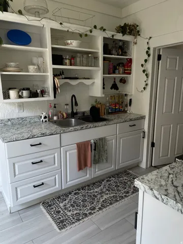 Kitchen featuring white shaker-style cabinetry, patterned stone countertops, and a dual basin sink with a matte black faucet