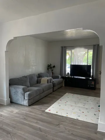Spacious room featuring wood-finish flooring, a large window with natural light, and an arched entryway