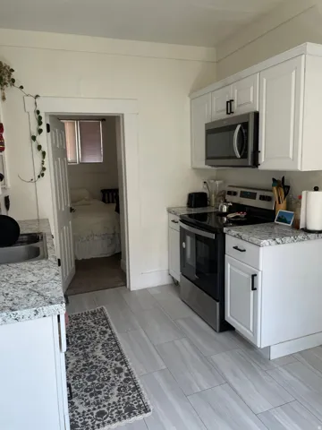 Kitchen featuring white shaker cabinetry, stainless steel appliances, granite countertops, and wood-finish tile flooring